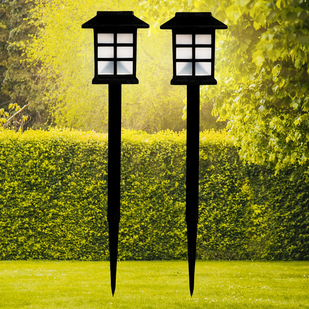 A pair of sleek black solar garden lights illuminating a lush green lawn at dusk.