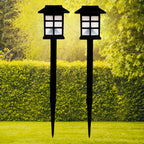 A pair of sleek black solar garden lights illuminating a lush green lawn at dusk.