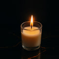 A lit Scented Votive Candle in a clear glass jar, casting a warm glow.