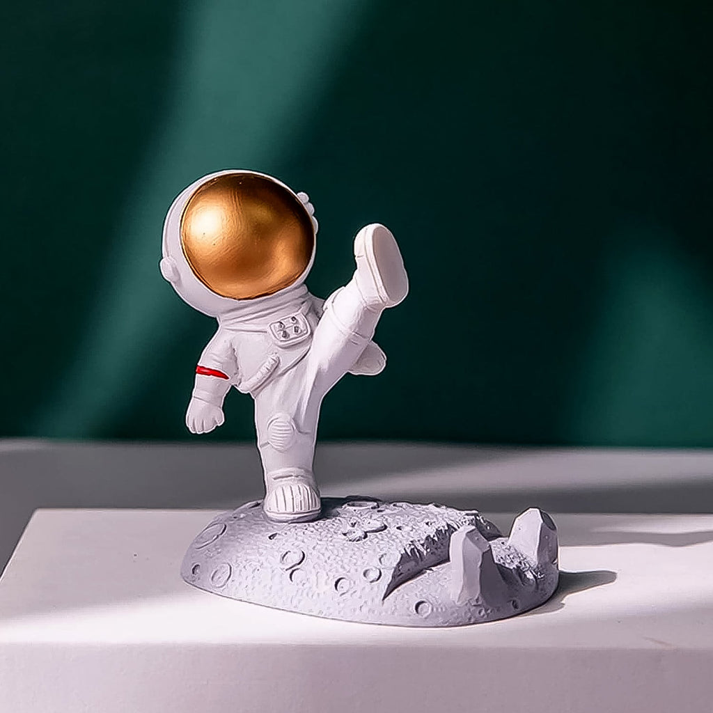 Astronaut Phone Holder (kicking leg design) on a wooden desk, holding a smartphone.