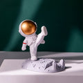 Astronaut Phone Holder (kicking leg design) on a wooden desk, holding a smartphone.