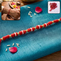 Red thread rakhi with white pearl beads and golden accents