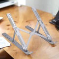 A person uses a silver metal portable laptop stand with a laptop on a desk.