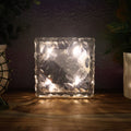 A single ice cube shaped solar garden light glowing warmly on a dark surface.