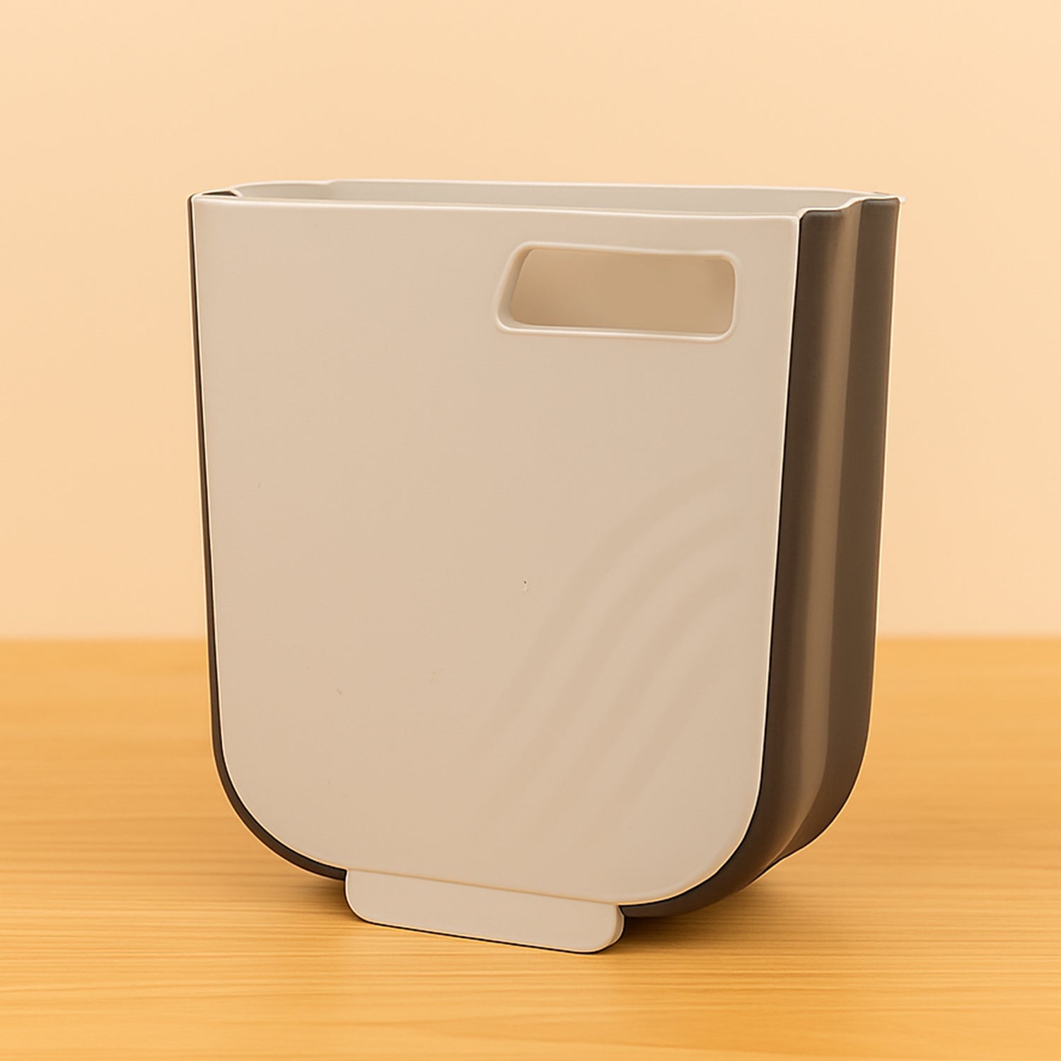 Collapsible hanging trash can mounted on a kitchen cabinet door, collecting food waste.