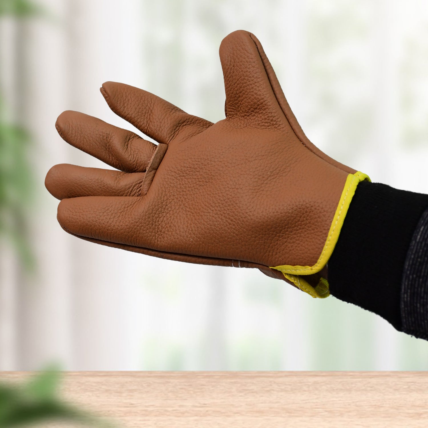 Gardener wearing brown and green leather gloves, tending to plants in a sunny garden.