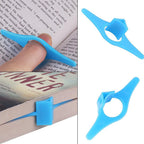 White thumb book support keeping a book open on a desk, next to a cup.