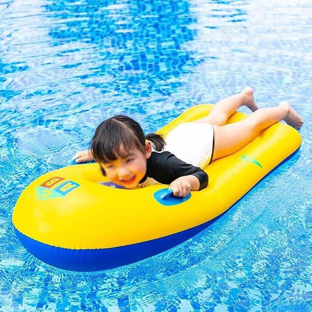 Child happily riding a yellow inflatable surfboard with handles in clear blue water.