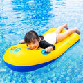 Child happily riding a yellow inflatable surfboard with handles in clear blue water.