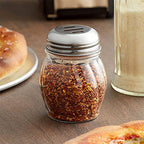 Oregano & Chilli flakes spice shakers placed on dining table with fresh herbs