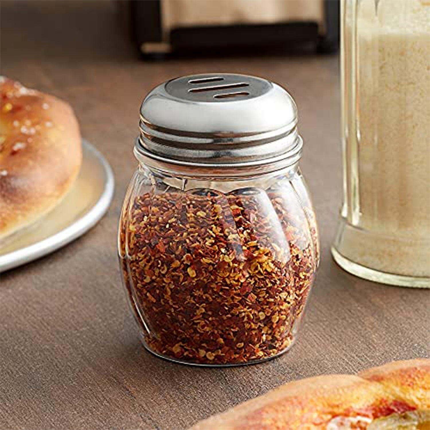 Oregano & Chilli flakes spice shakers placed on dining table with fresh herbs
