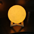 A beautifully lit 3D moon lamp with touch controls on an elegant crystal ball stand.