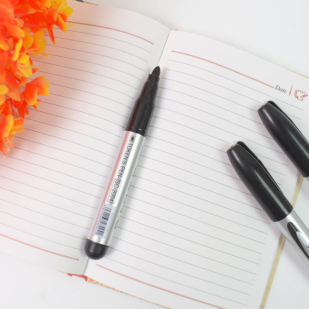 Four black markers displayed on an office desk alongside other stationery items.