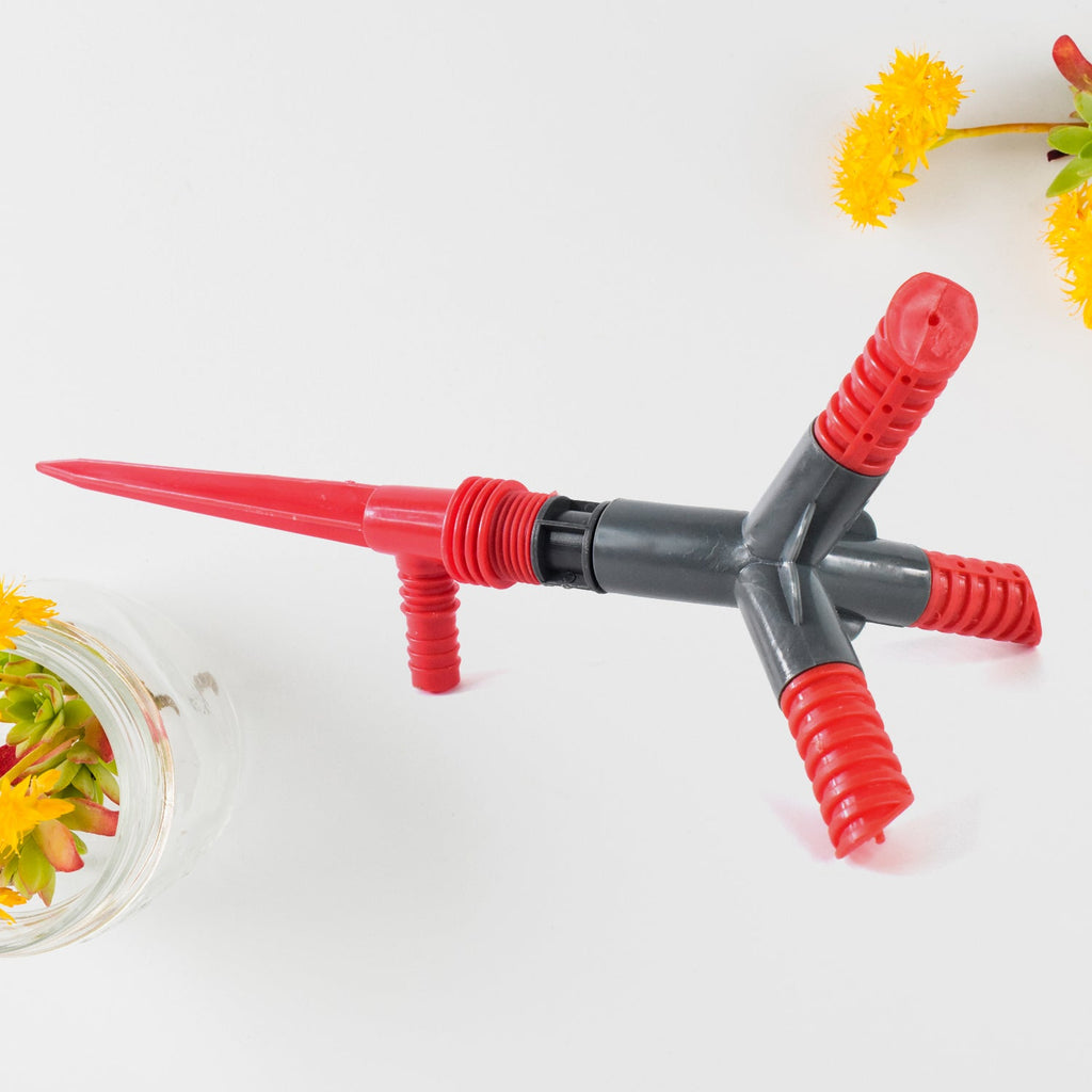 Rotating garden sprinkler connected to a hose, actively spraying water on a lawn.