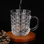 Person enjoying a hot beverage in a stylish glass coffee mug.