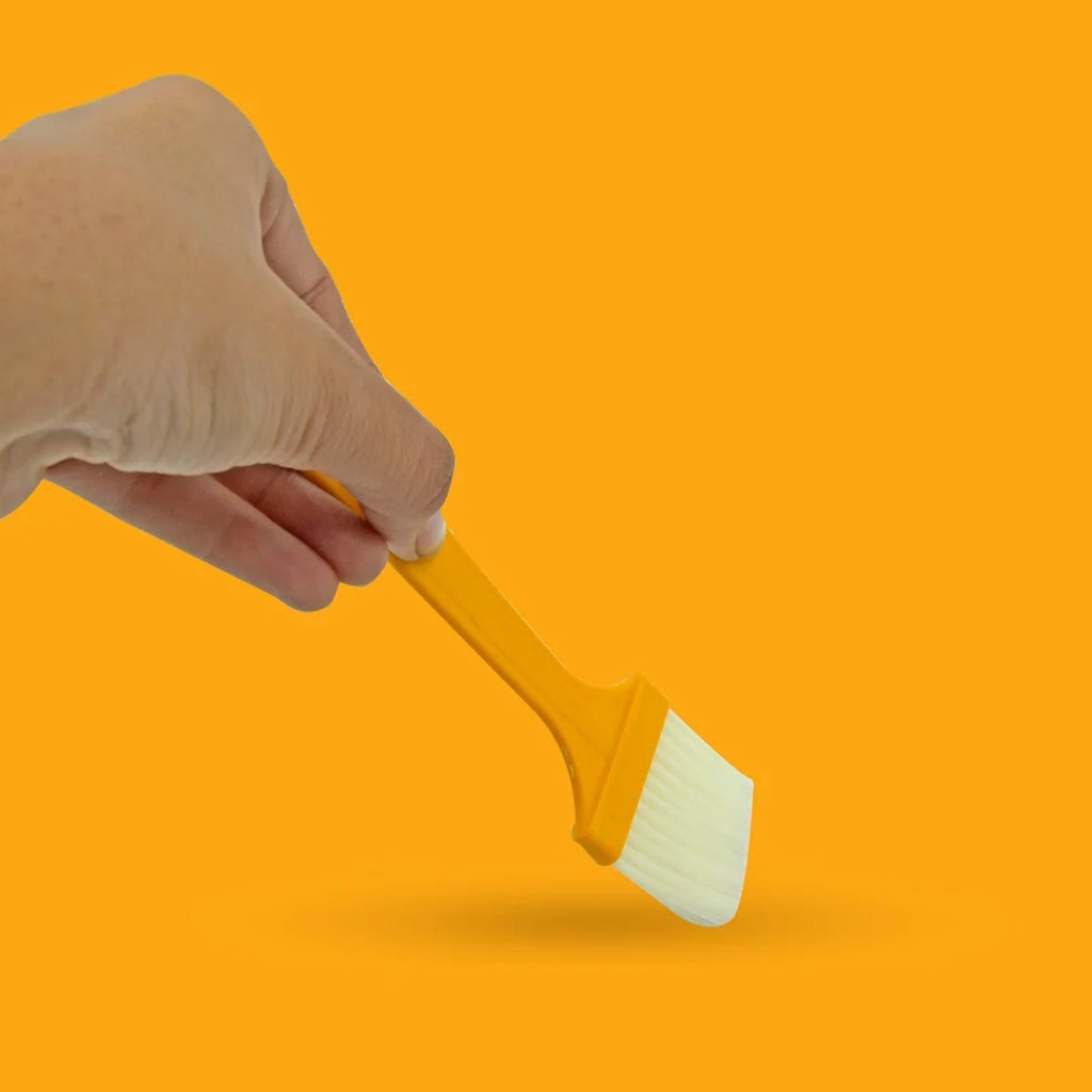 A hand holding one of the silicone basting brushes, ready for use in a kitchen.