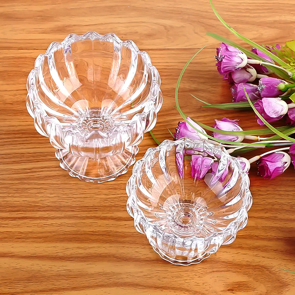 Six clear glass dessert bowls arranged on a table with spoons, ready for serving.