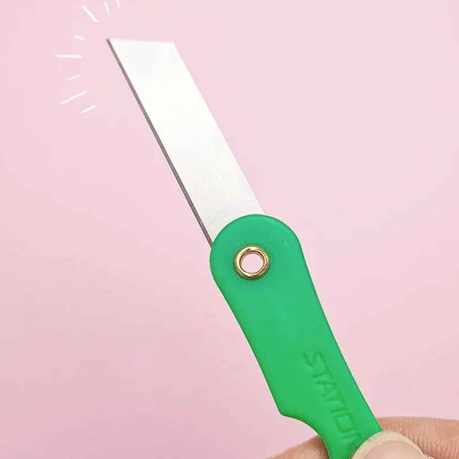 Hand holding a multicolour mini paper cutter knife, demonstrating its compact size.