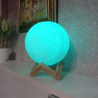 A blue LED night light shaped like the moon, resting on its plastic base.
