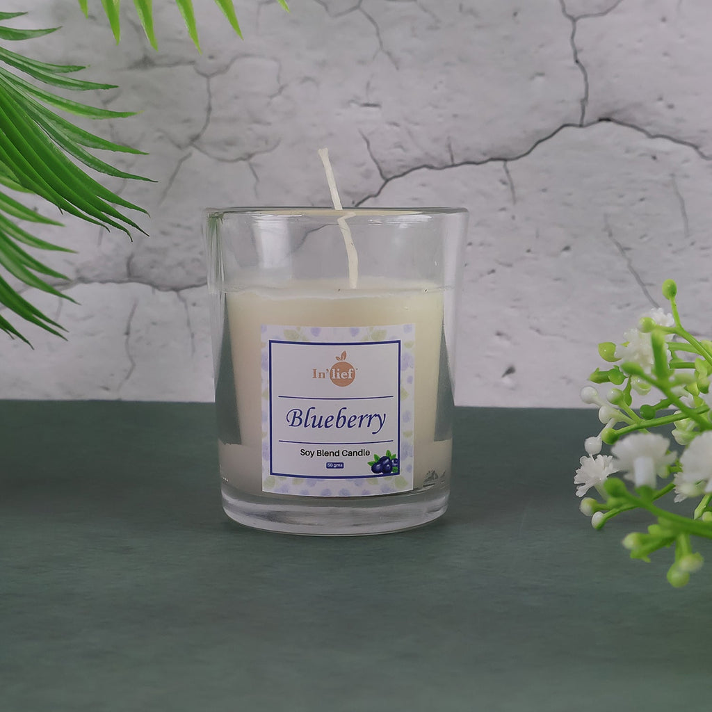 Lit Blueberry Scented Candle with fresh blueberries scattered around it, enhancing the aroma theme.