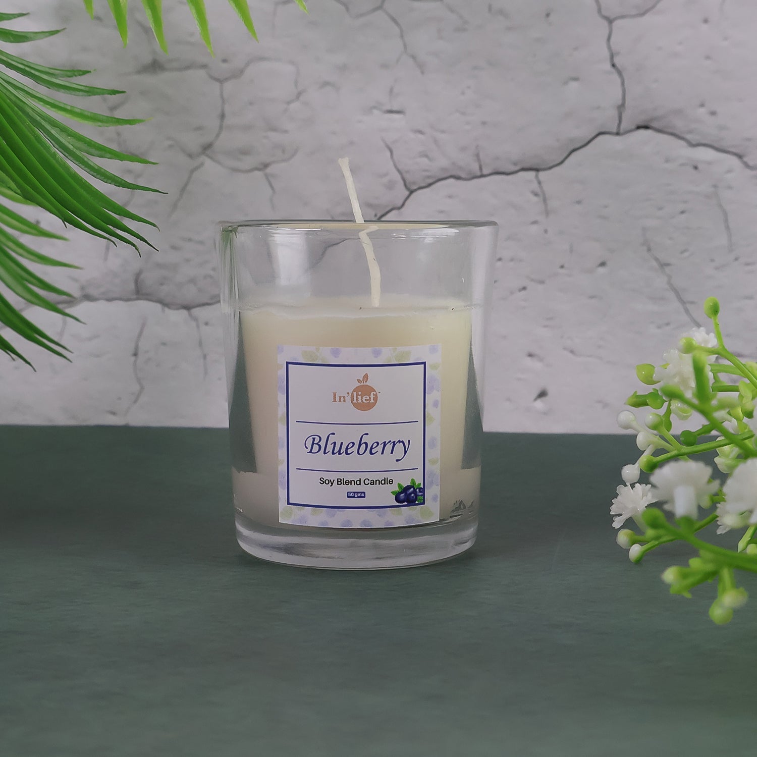 Lit Blueberry Scented Candle with fresh blueberries scattered around it, enhancing the aroma theme.