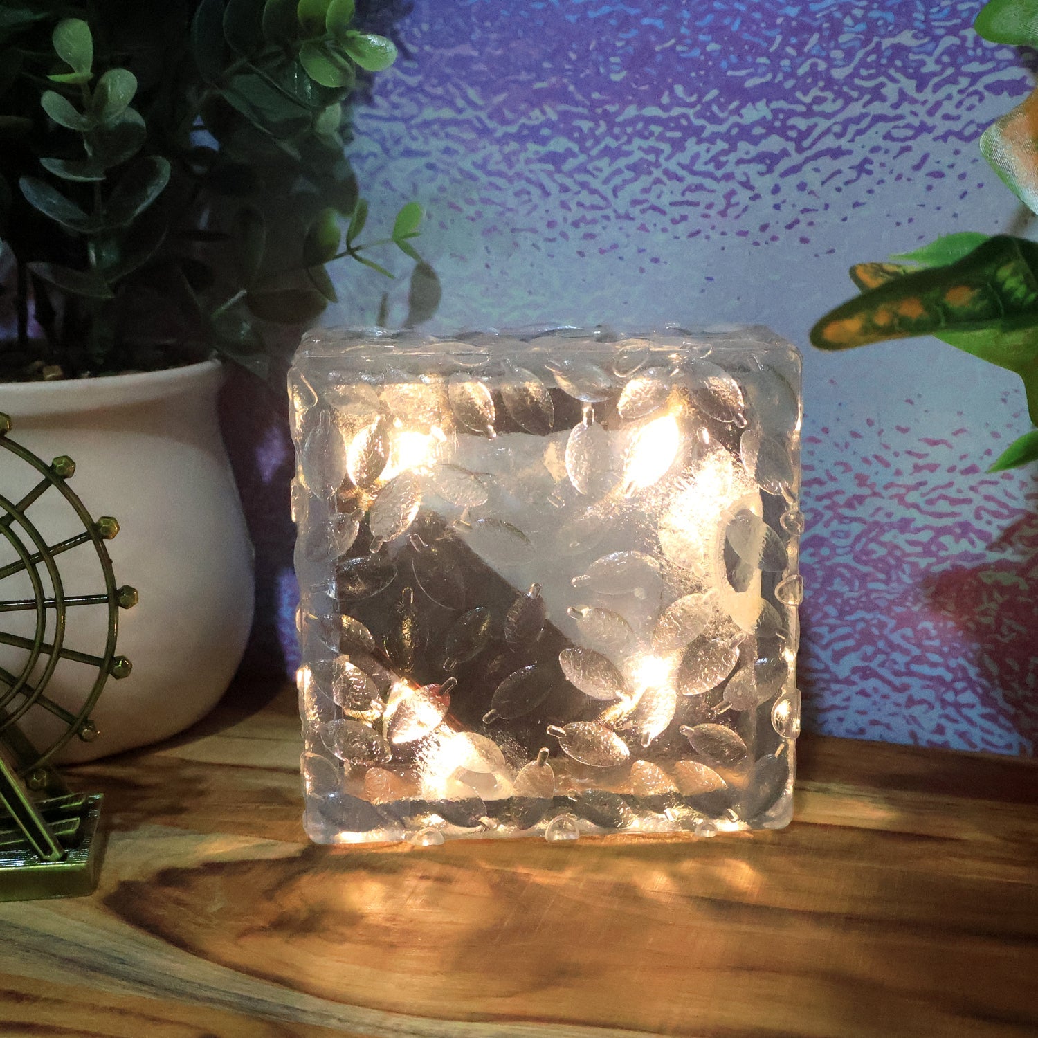 An ice cube solar light casting a soft glow on green foliage in a garden.