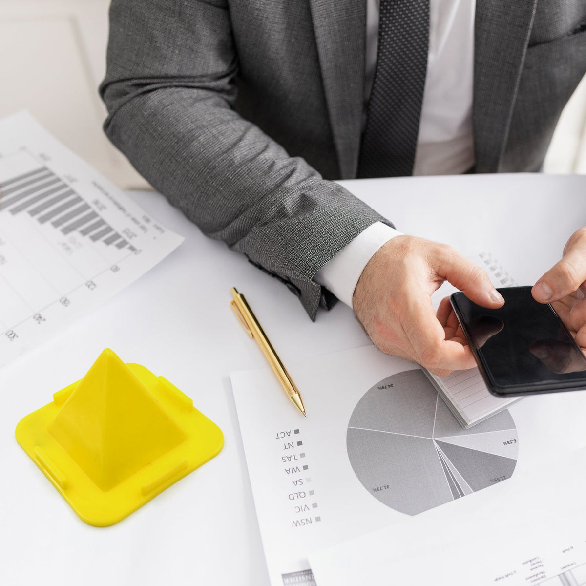 A flexible pyramid mobile stand in black, holding a smartphone upright on a desk.