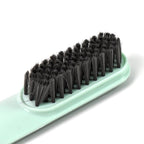 The small cleaning brush displayed next to a pair of shoes, highlighting its size.
