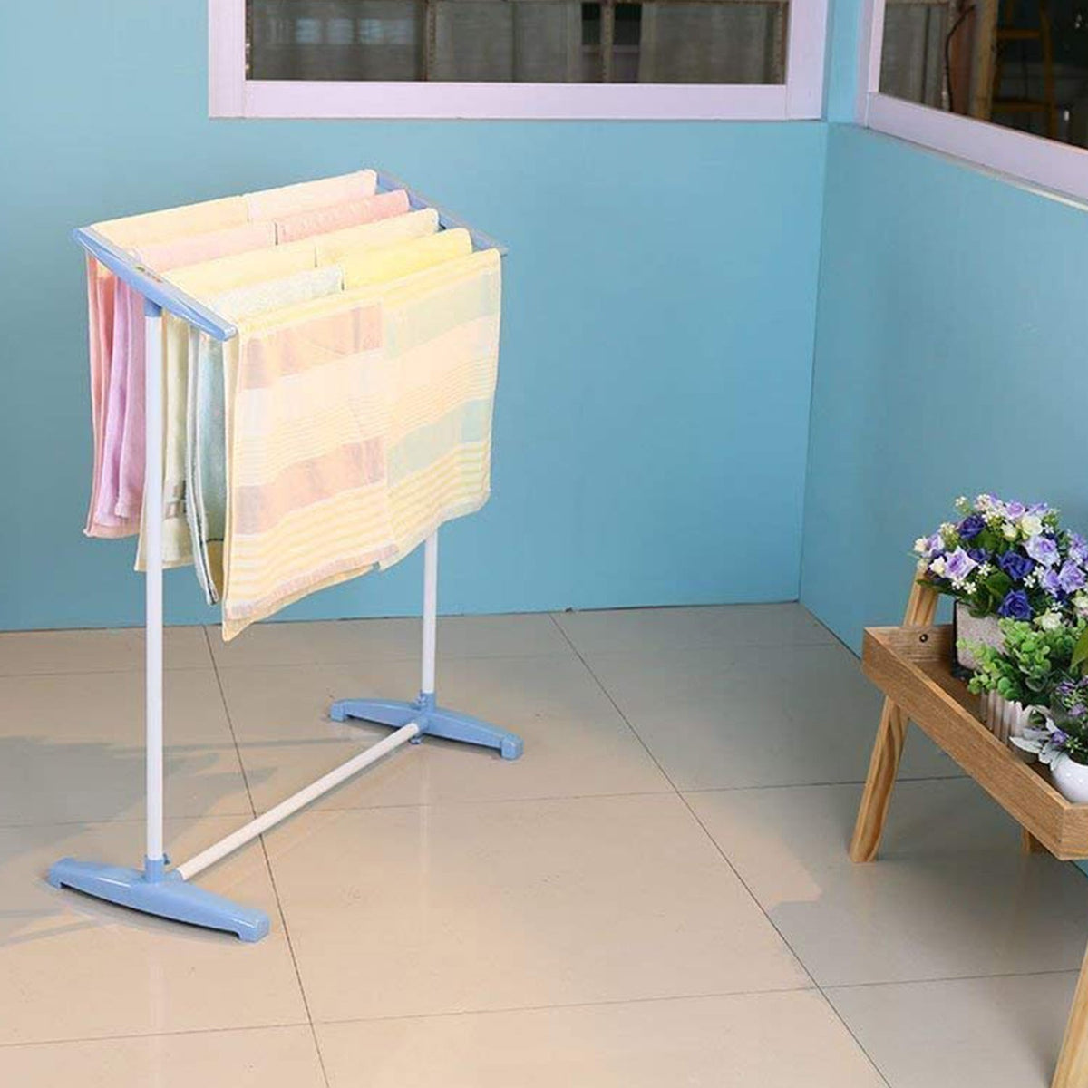 Portable clothes drying rack with towels and clothes in a balcony setting.