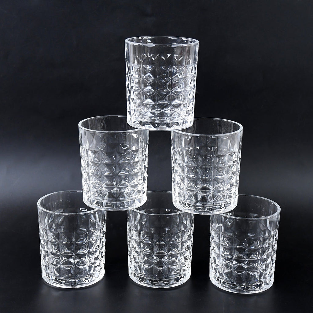 Three diamond-cut glass tumblers filled with different beverages on a wooden surface, ready for serving.