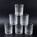 Three diamond-cut glass tumblers filled with different beverages on a wooden surface, ready for serving.