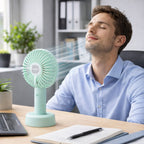 Portable handheld fan cooling a user at an office desk, perfect as a personal cooling device.