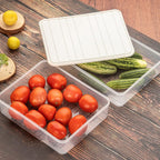 A transparent plastic vegetable storage box with a blue lid, shown filled with various fresh vegetables.