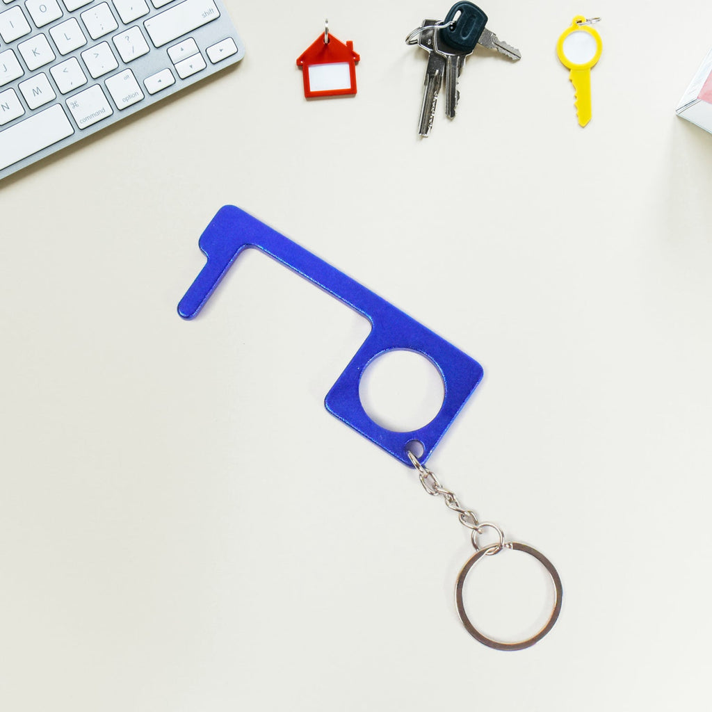 Hand holding Safe Touch Tool metal keychain used for hygienic door opening
