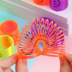 A child's hand holding a rainbow slinky spring toy over a wooden table.