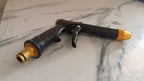 Brass water spray gun attached to a hose, powerfully spraying water during outdoor cleaning.