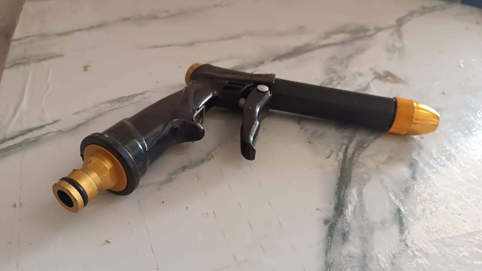Brass water spray gun attached to a hose, powerfully spraying water during outdoor cleaning.