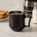 Black plastic coffee mug with handle on a white background, perfect for daily use.