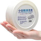 Hand applying Velvet Wipe shoe stain remover cream with a sponge on a white shoe.