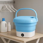 Portable folding washing machine in a kitchen setting with a basket of clothes.