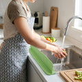 Flexible silicone kitchen sink splash guard protecting countertop during vegetable washing.