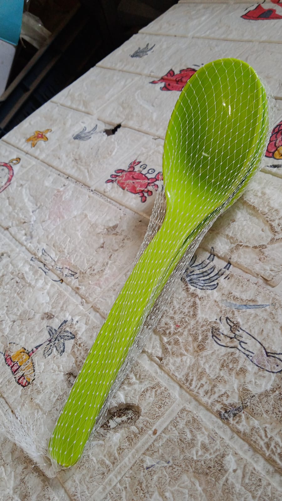 Single black plastic kitchen ladle resting on a rustic wooden table, ready for use.
