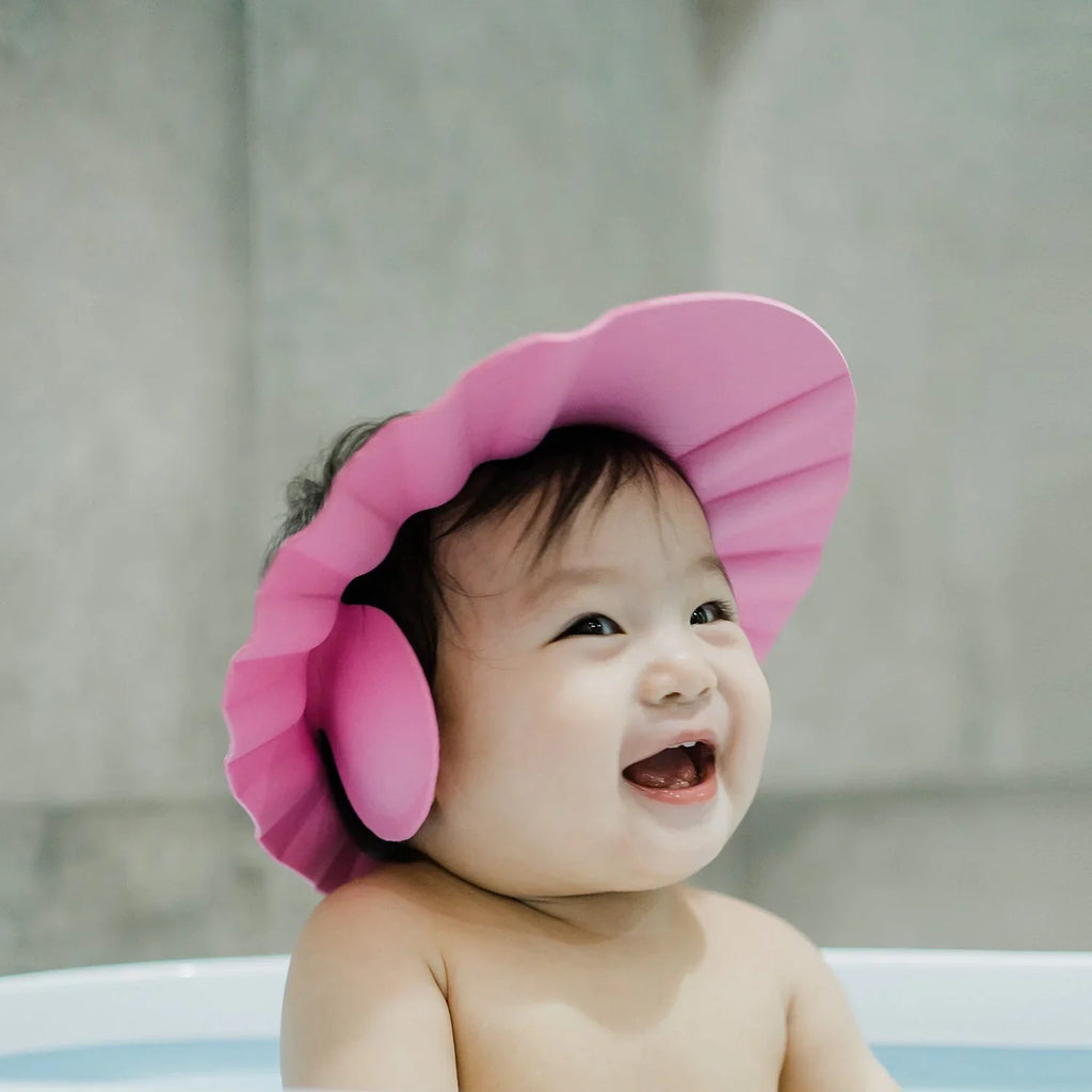 Pink baby shower cap with adjustable strap, designed for splash-proof hair washing.