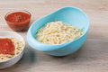 Large plastic rice bowl strainer in use, showing grains being washed.