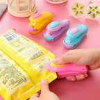 User actively sealing a blue plastic bag with the portable mini food sealer.
