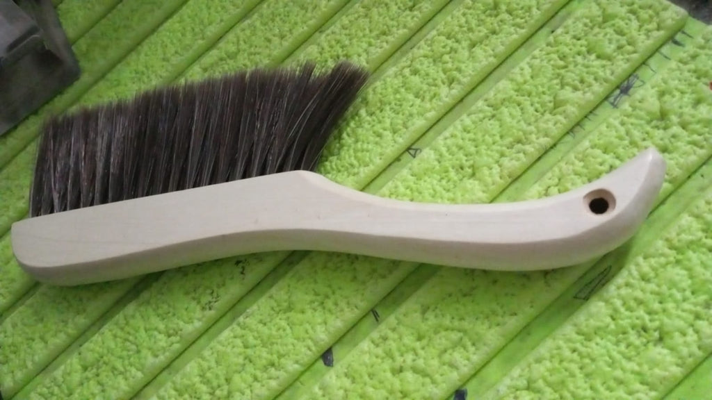 Hand holding a soft bristle brush, gently cleaning a sofa surface to remove dust.