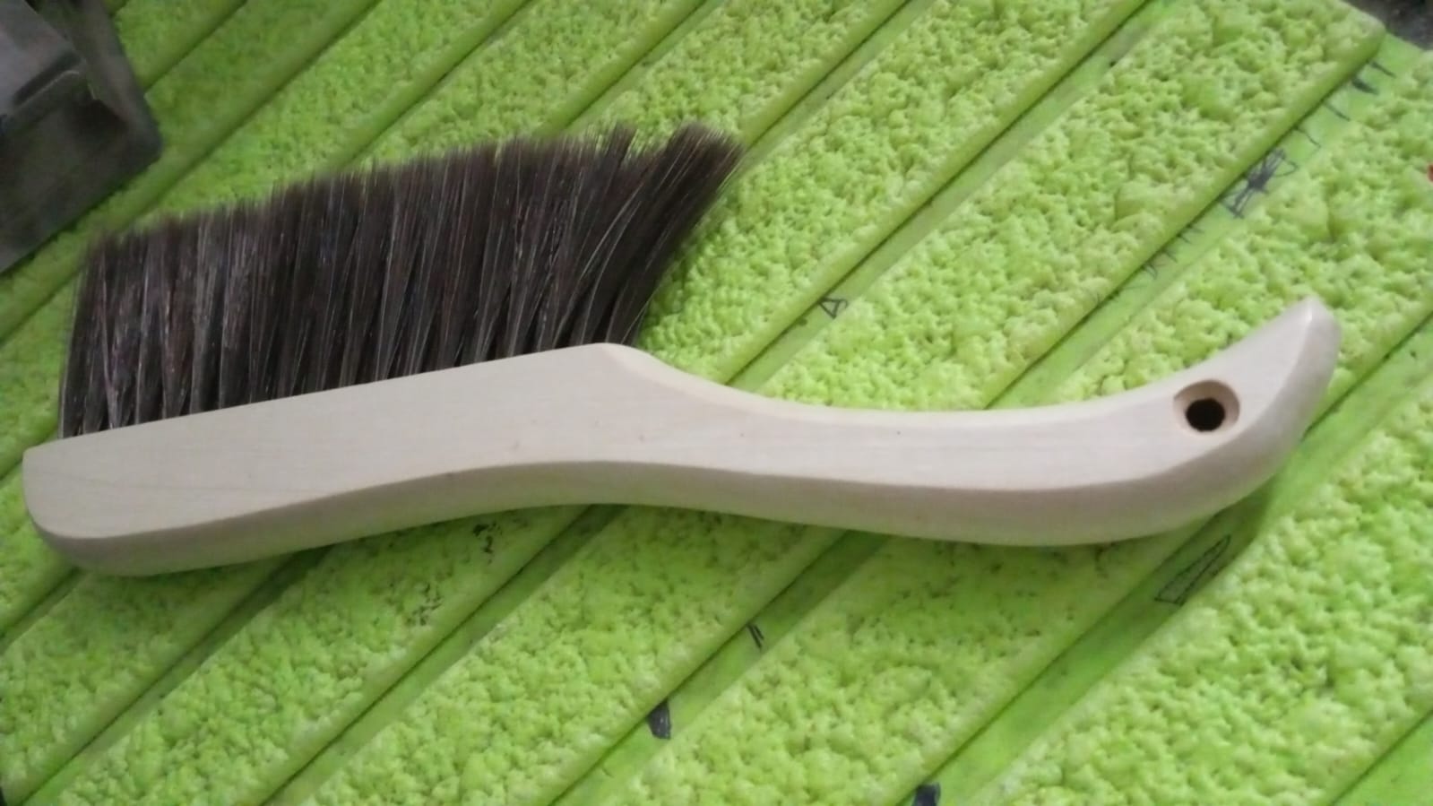 Hand holding a soft bristle brush, gently cleaning a sofa surface to remove dust.