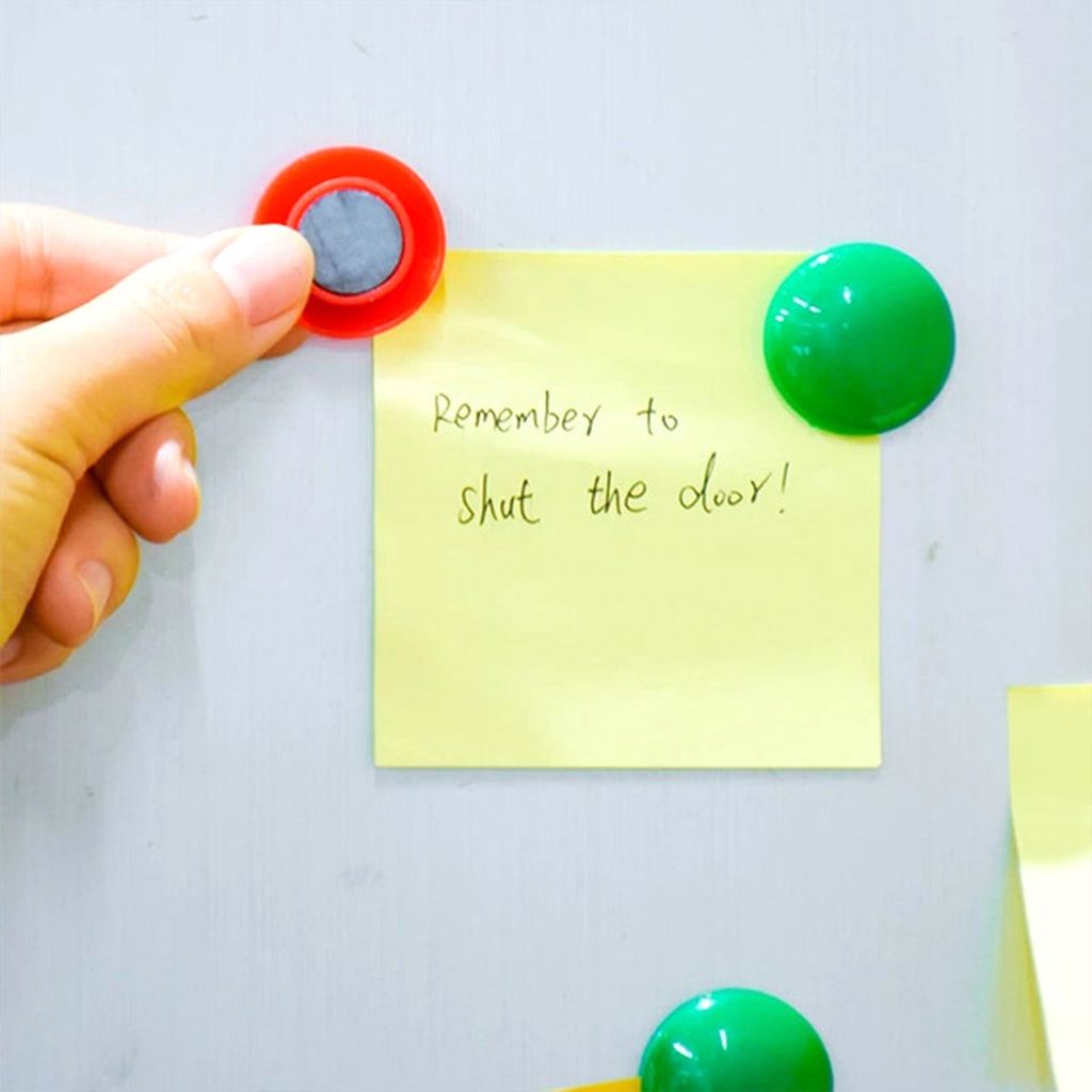 Colorful board magnets holding papers on a white magnetic surface.