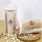 A transparent 4 section kitchen storage jar with a red lid, filled with various dry foods like cereals and pulses, by Organivo.