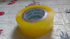 Transparent packing tape roll unwound slightly, showing its strong adhesive side.